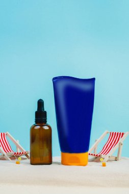 Yaz kremi reklamları. Plaj tatil kozmetik ürünleri. Güneş kremi ve güneş özü. Unisex kozmetik. Kumsalda dinlenmenin konsept fotoğrafı. Mavi arka planda, kumsaldaki güverte sandalyeleri. Model 