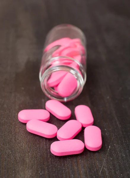 Pink pills an pill bottle on black table — Stock Photo, Image