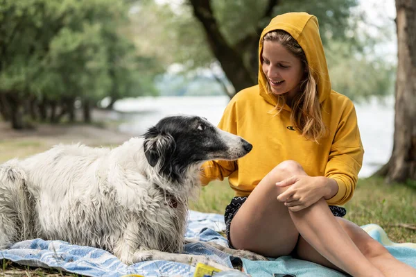 Young woman with Russian wolfhound dog resting outdoor in forest at the river