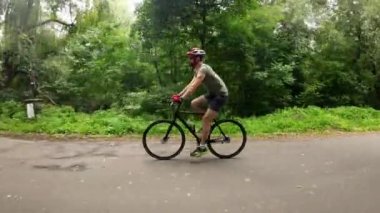 Man in protective helmet with action camera attached on it ride on bicycle in the park.