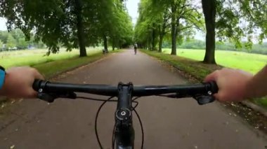 Point of view of man cycling on along the asphalt path in the park. POV