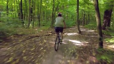 Young man in a bicycle helmet rides a bicycle through the forest. Following Shot 