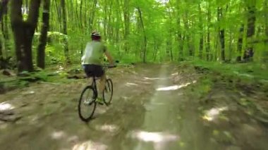 Young man in a bicycle helmet rides a bicycle through the forest. Following Shot 