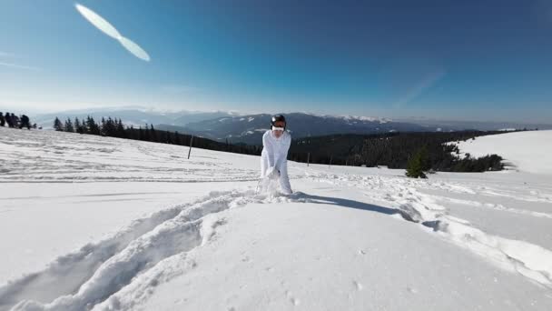 白いスキースーツの女が雪に覆われた山々の背景を背景に雪を投げます スローモーション — ストック動画