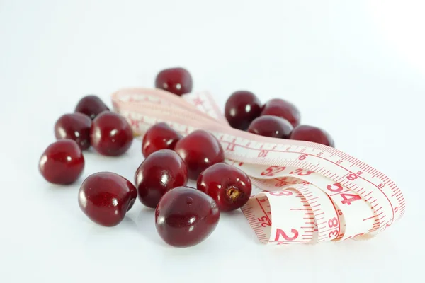 Dieta e nutrição. Cerejas com fita métrica sobre fundo branco — Fotografia de Stock