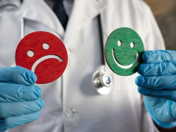 Patient satisfaction survey. Doctor holds joyful and sad emoticons. — Stock Photo, Image
