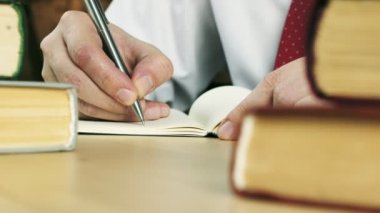 Close-up of hands writing in a notebook at the table with books.