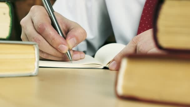 Крупним планом руки пишуть в блокноті за столом з книгами . — стокове відео