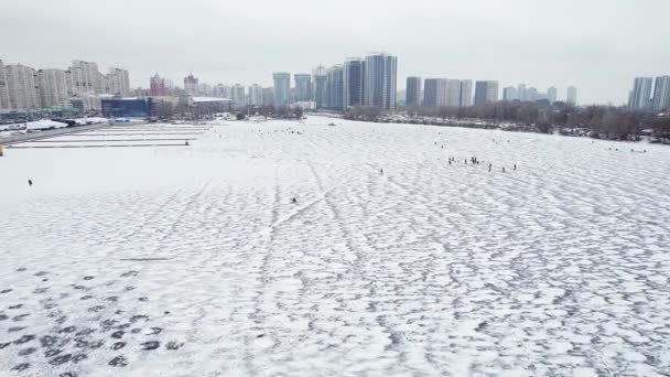 Flying over a frozen river with unrecognizable fishermen in winter. City landscape. — Stockvideo