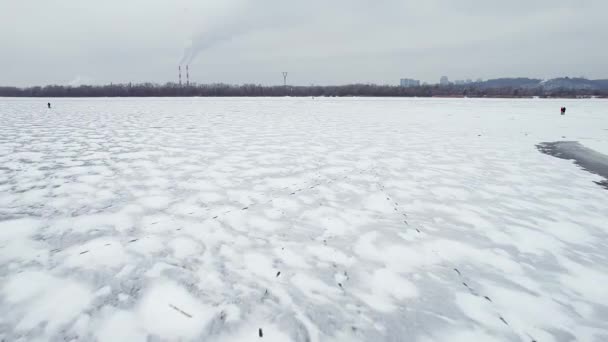 Flying over a frozen river in the direction of smoking industrial chimneys. Unrecognizable people. — Stockvideo