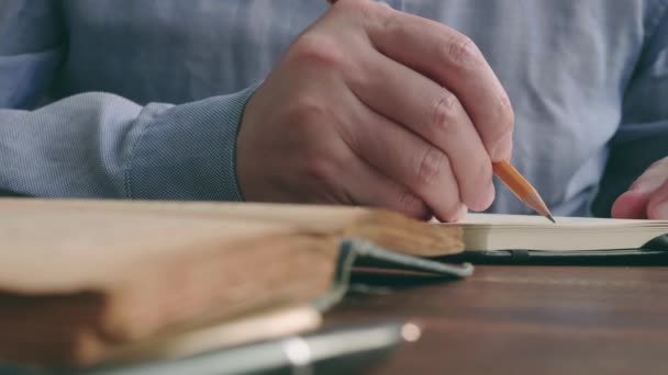 Close-up of a male hand writing with a pencil in a notebook next to an old book. Knowledge and wisdom. — Stockvideo