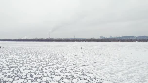 Überflug eines gefrorenen Flusses mit rauchenden Schloten am Ufer und Menschen auf dem Eis. — Stockvideo