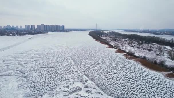 Вид с воздуха на замерзшую реку с мостом и городскими зданиями на берегу. — стоковое видео