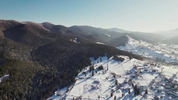 Schneebedeckte Berge und ein Dorf auf einem Hügel. Luftaufnahme. — Stockvideo
