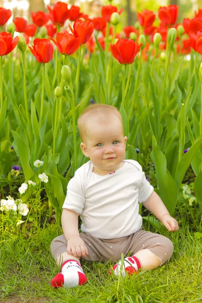 Jonge schattige vrolijke baby sit in park op groen gras en spelen — Stockfoto