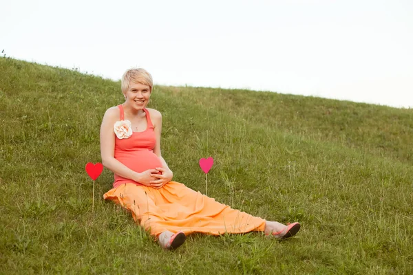 Mulher grávida desfrutando de parque de verão segurando um papel coração vermelho, o — Fotografia de Stock