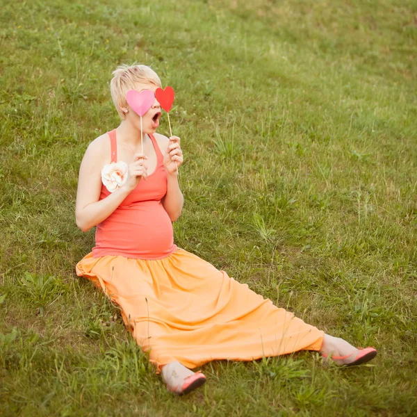 Pregnant woman enjoying summer park holding a paper red heart, o Royalty Free Stock Photos