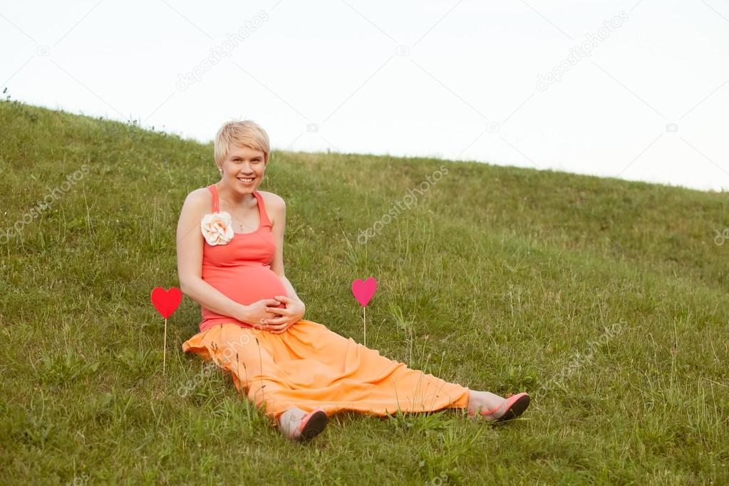 pregnant woman enjoying summer park holding a paper red heart, o