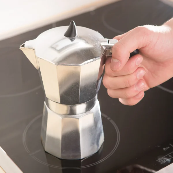 Italienische Kaffeekanne in der Hand auf einem schwarzen Elektroherd. — Stockfoto