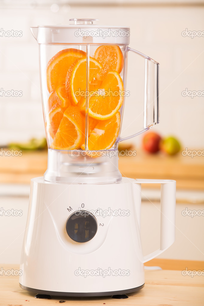 White blender with juicy oranges on a wooden table