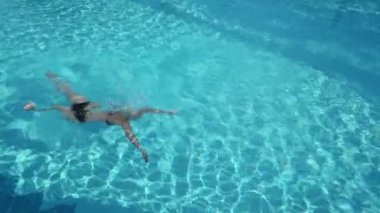 Havuza dalıp su sıçratan aktif genç bir kadın. Tropikal tatil beldesinde dinlenen bayan.