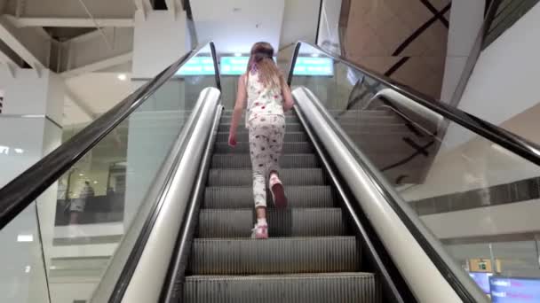 Visszapillantás a kislányra, aki felköltözik a mozgólépcsőn. — Stock videók