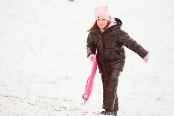 Šťastná holčička sjíždí z kopce na talířových saních. Dívka těší jezdec jízda na sněhu — Stock fotografie