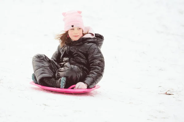 Gelukkig meisje glijdt van de heuvel af op schotelslee. Meisje genieten slider rit op de sneeuw — Stockfoto