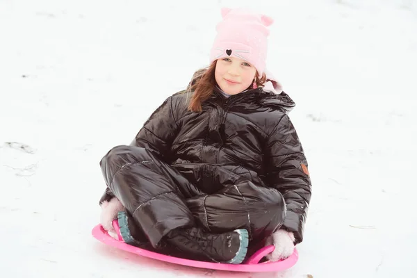 Glückliches kleines Mädchen, das auf einem Untersetzerschlitten den Hügel hinuntergleitet. Mädchen genießen Rutschpartie auf dem Schnee — Stockfoto