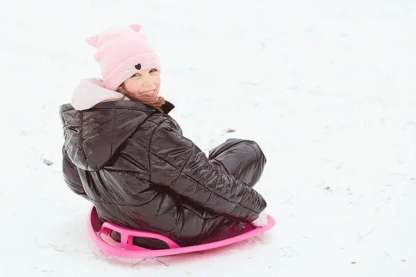 Glückliches kleines Mädchen, das auf einem Untersetzerschlitten den Hügel hinuntergleitet. Mädchen genießen Rutschpartie auf dem Schnee — Stockfoto