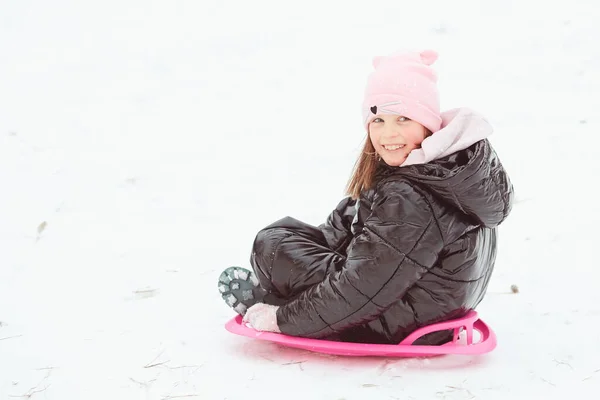 Ευτυχισμένο κοριτσάκι που κατεβαίνει το λόφο με έλκηθρο. Κορίτσι απολαμβάνει βόλτα με το έλκηθρο στο χιόνι — Φωτογραφία Αρχείου