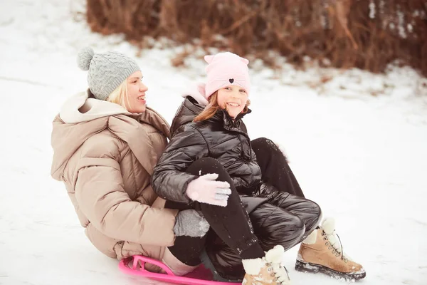 Glückliche Mutter mit Baby-Mädchen auf Schlitten sitzend und Schlitten auf Schnee von Hügel hinunter. Weiße Wintertage im Park genießen. Gemeinsam Zeit am Wochenende verbringen. — Stockfoto