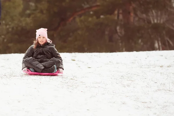 Aktives Mädchen rutscht den Hügel hinunter. Glückliches Kind, das sich im Winter draußen auf dem Schlitten vergnügt. Familienzeit. — Stockfoto