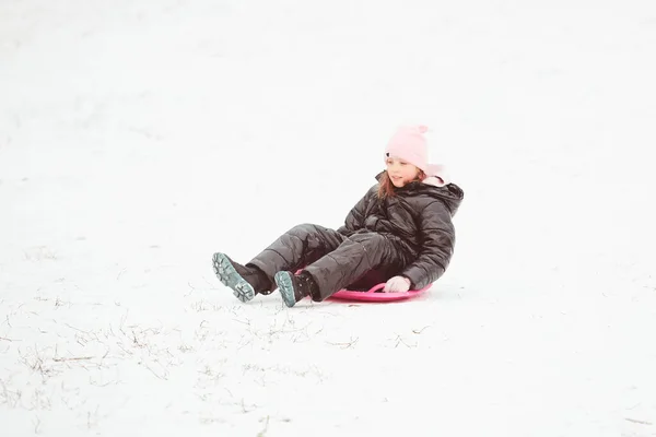 Aktivní dívka sjíždí z kopce. Šťastné dítě baví venku v zimě na saních. Rodinný čas. — Stock fotografie
