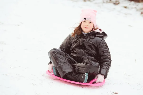 Actief meisje glijdt van de heuvel af. Gelukkig kind heeft plezier buiten in de winter op slee. Gezinstijd. — Stockfoto