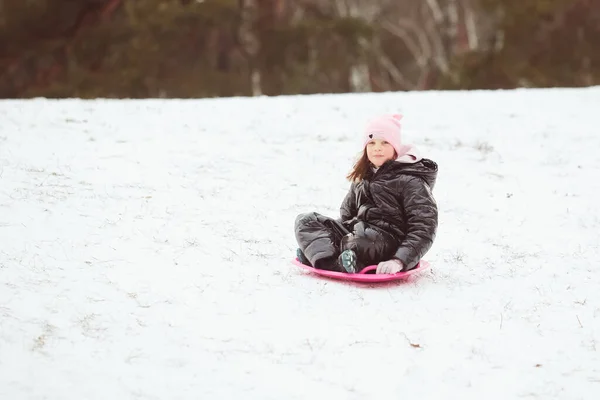 Aktywna dziewczyna zjeżdżająca ze wzgórza. Szczęśliwe dziecko bawiące się na świeżym powietrzu w zimie na sankach. Czas rodzinny. — Zdjęcie stockowe