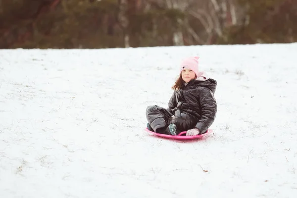 Actief meisje glijdt van de heuvel af. Gelukkig kind heeft plezier buiten in de winter op slee. Gezinstijd. — Stockfoto