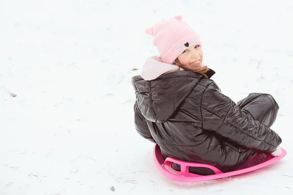 Ενεργό κορίτσι κατεβαίνει το λόφο. Ευτυχισμένο παιδί που διασκεδάζει έξω το χειμώνα με έλκηθρο. Οικογενειακός χρόνος. — Φωτογραφία Αρχείου