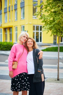 İki bayan arkadaş dışarıda gülüyor ve sarılıyorlar..