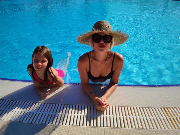 Joyeux petite fille avec mère dans un grand chapeau de paille quand ils se reposent à la piscine de l'hôtel spa — Photo