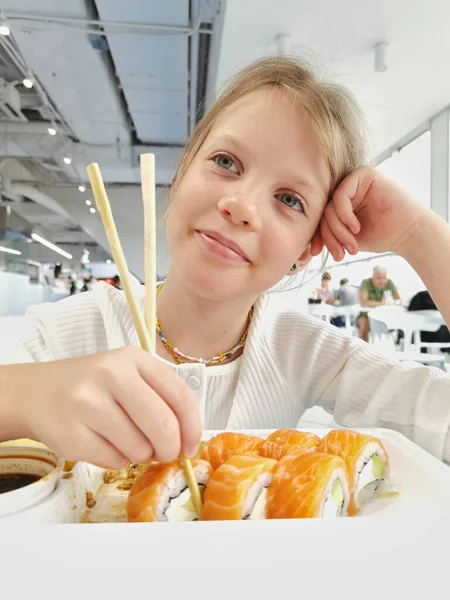 Linda niña sonriente con sushi. Niña comiendo sushi y rollos - concepto comercial. — Foto de Stock