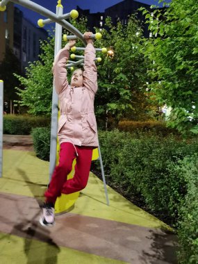 Aktif bir çocuk, 8-9 yaşlarında bir kız spor sahasında oynuyor, dengesiz barlara asılıyor..