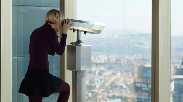 Woman tourist is looking through binoculars on city from a high point. — Foto Stock