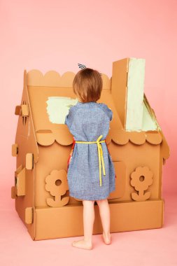 Karton evi çizen ve evde eğlenen kızın yan görüntüsü..