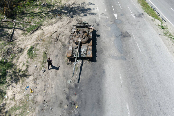 Kyiv region, Ukraine - May 15, 2022: War in Ukraine. Highway Kyiv - Zhytomyr. People take selfies against destroyed russian tank after russian atack in Febrary.