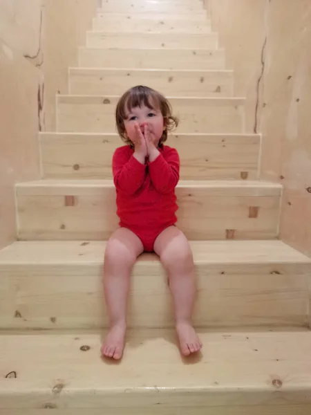 面白いです幼児赤ちゃん女の子で赤い体に座っています上の階段室内 — ストック写真