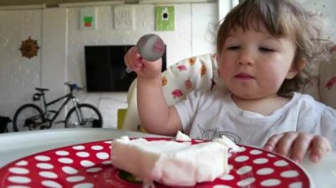 Dağınık ağızlı ve suratlı neşeli bir kız bebek yemek. Bir yaşındaki çocuk yer ve güler. Mutlu, tapılası çocuk tatlı yer ve zevkle bağırır. Küçük komik çocuk portresi ve mutfakta yemek..