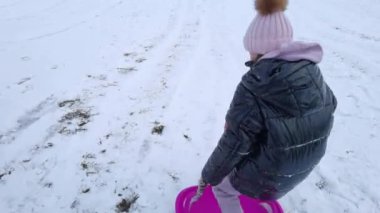 Kız karda eğleniyor, plastik kürek kızağıyla kaymanın zevkini çıkarıyor..