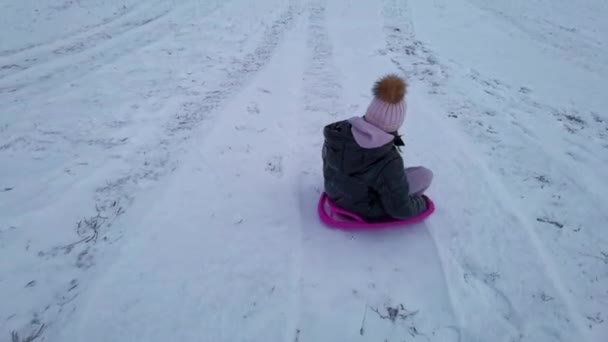 雪の上で楽しみ プラスチック製のシャベルそりを使用してそりの楽しさを楽しんでいる女の子 — ストック動画