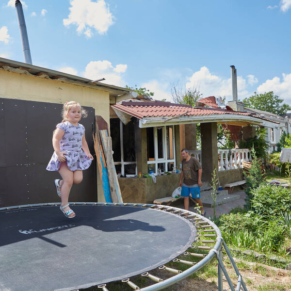 Chernihiv, Ukraine - June 26, 2022: Girl jumps on batute, against her destroyed house. Resident of the Chernihiv, whose house was completely destroyed by russian artillery.